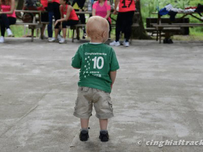 Bambino con maglietta verde e numero 10 su schiena, al centro di un'area all'aperto.