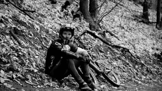 Ciclista in scarico su sentiero di montagna, abbigliamento tecnico e casco, nel bosco autunnale.