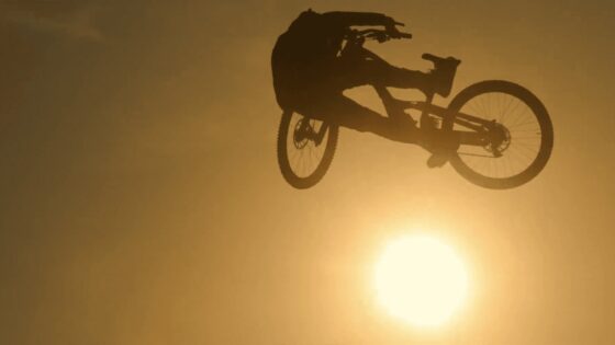 Ciclista in volo durante un salto con il sole sullo sfondo, scena dinamica di mountain biking.