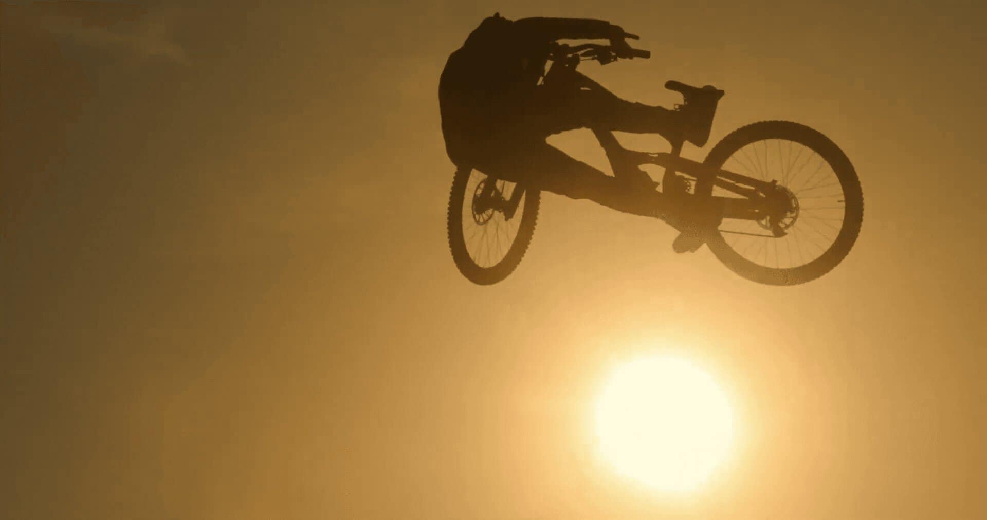 Ciclista in volo durante un salto con il sole sullo sfondo, scena dinamica di mountain biking.