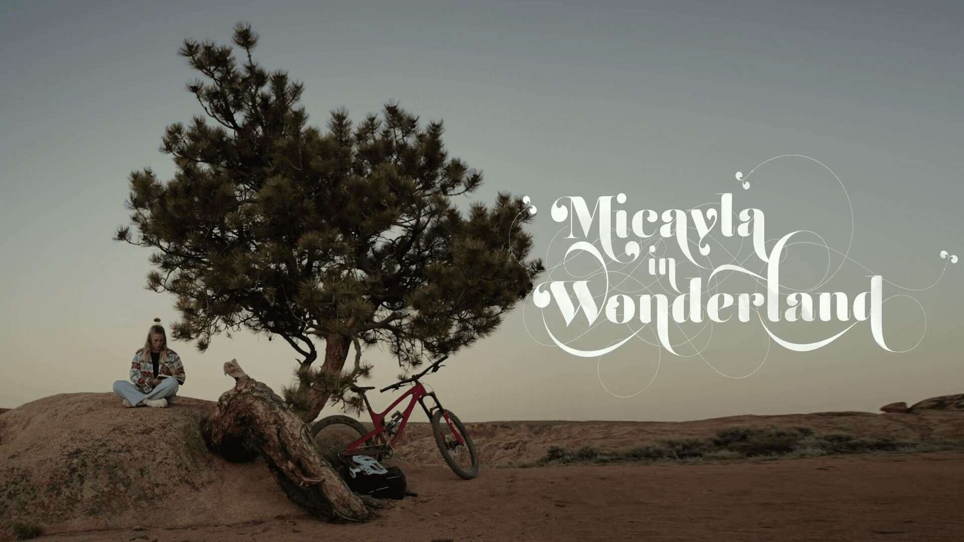 Calma e natura: ragazza seduta sotto albero con bici da montagna in paesaggio desertico.