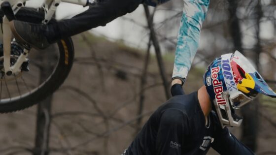 Casco con logo Red Bull e motociclista con MTB in un sentiero naturale.