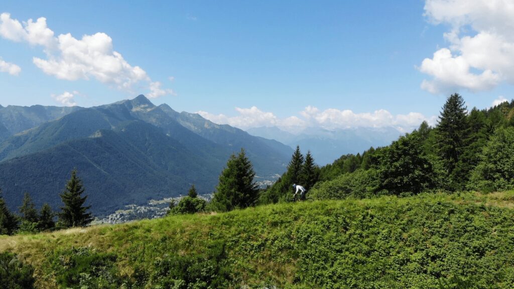 Suggestione di una cartolina di montagna con ciclista in azione tra le verdi pendici e le maestose vette sullo sfondo.