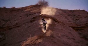 Pilota di mountain bike in discesa su terreni rocciosi con polvere nell'aria, avventura e adrenalina.