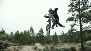 Salto in mountain bike su un sentiero di montagna con boschi e cielo nuvoloso.