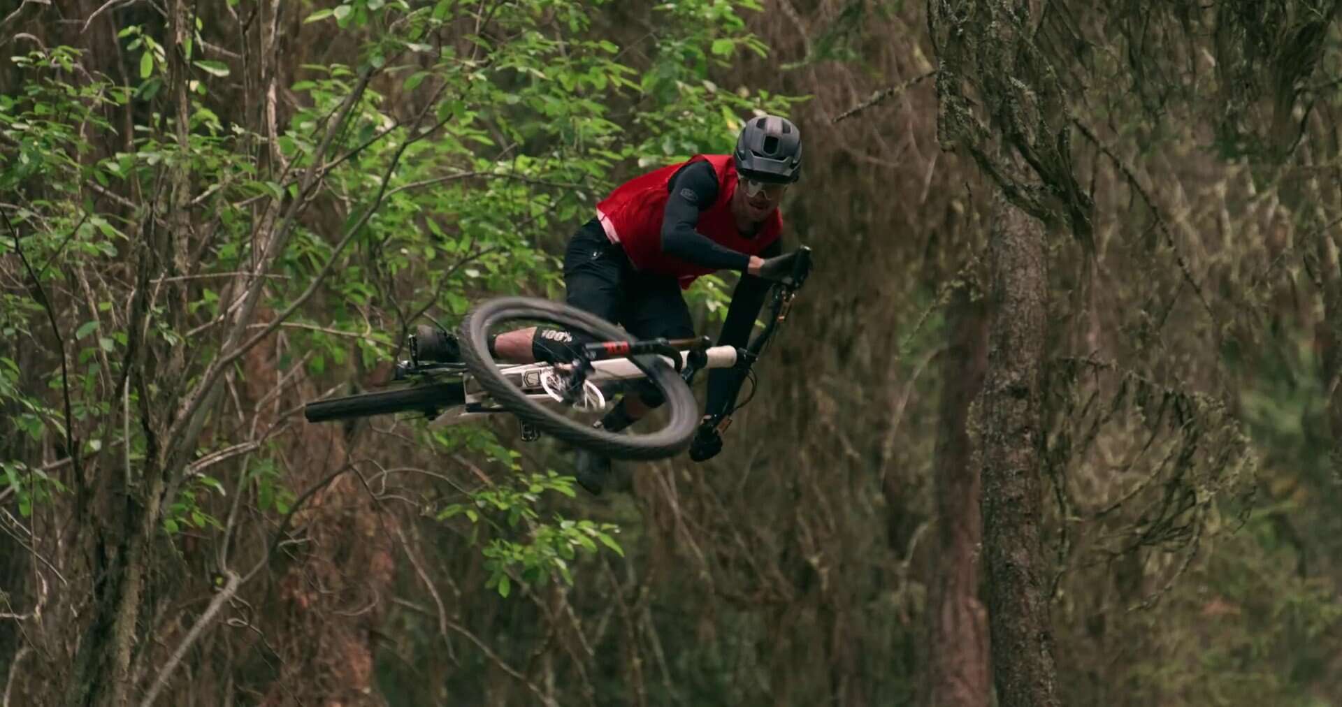 Salto di un ciclista in mountain bike tra gli alberi della foresta, stile avventura e adrenalina.