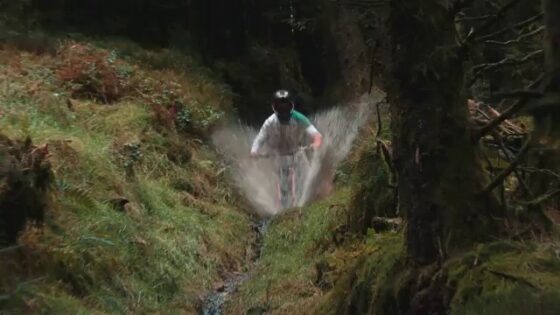 Ciclista su sentiero di montagna attraversando un piccolo ruscello nella natura.