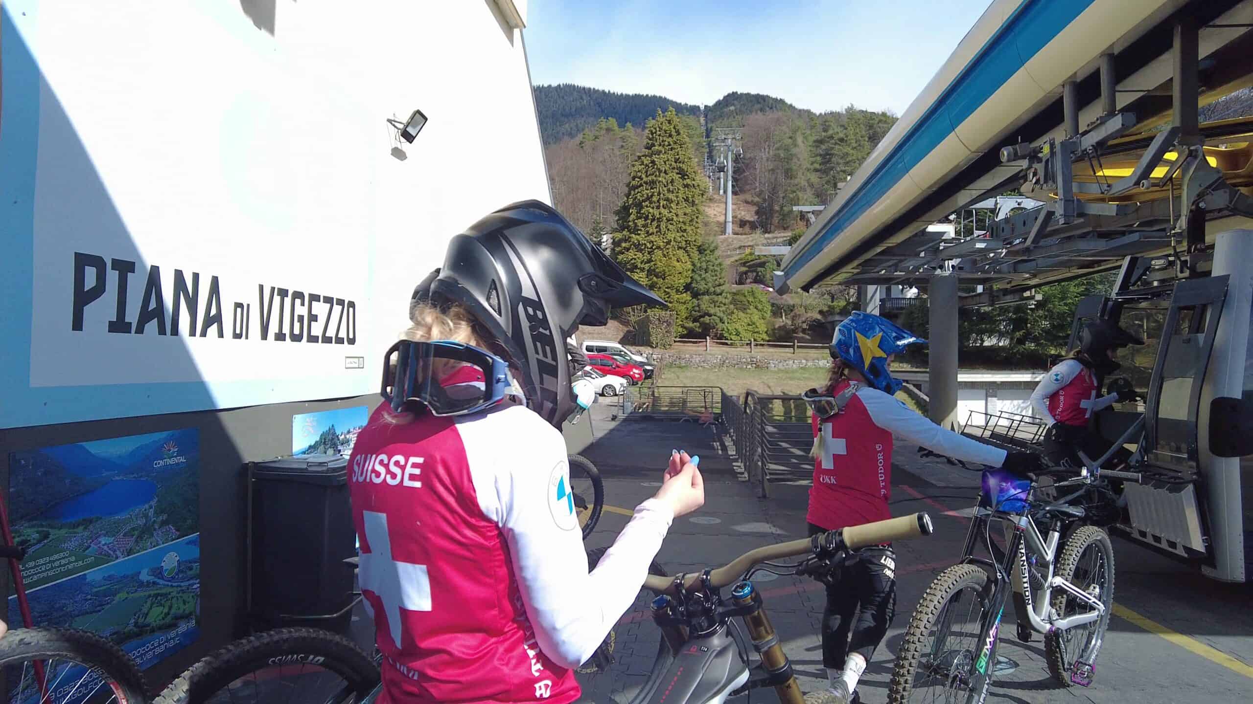 Grintaglio di mountain bike con ciclisti svizzeri pronto per partire, sullo sfondo montagne e funivie.