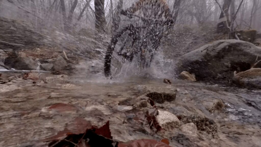 Acqua che scorre sui sassi, un ciclista attraversa un torrente di montagna.