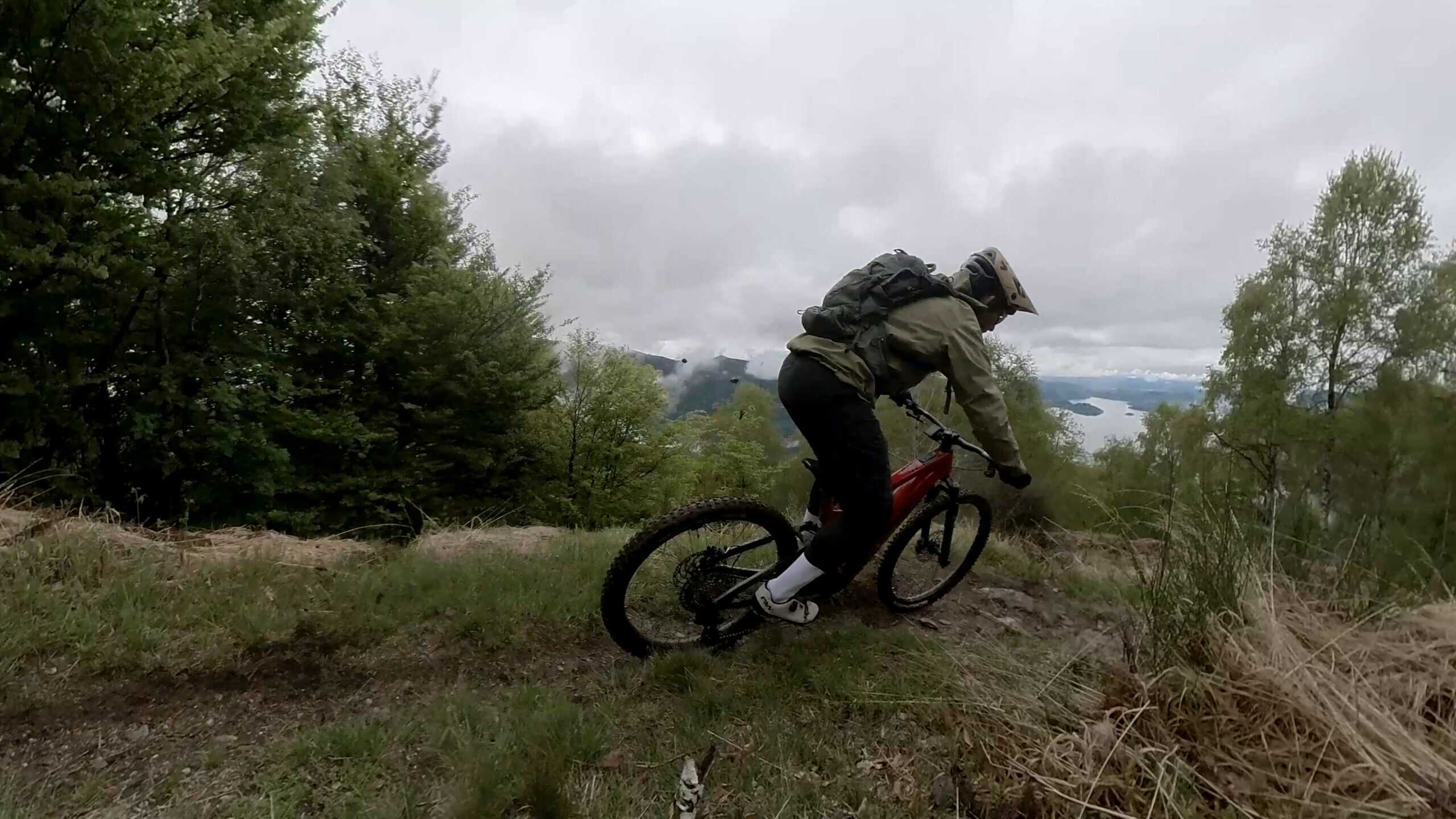 Escursionista su MTB in sentiero di montagna con vista lago, ambiente naturale, cielo nuvoloso, sport all'aperto e avventura.