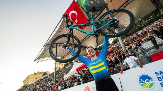 Atleta svedese solleva la bicicletta dopo una vittoria, pubblico entusiasta e arena di gara affollata.