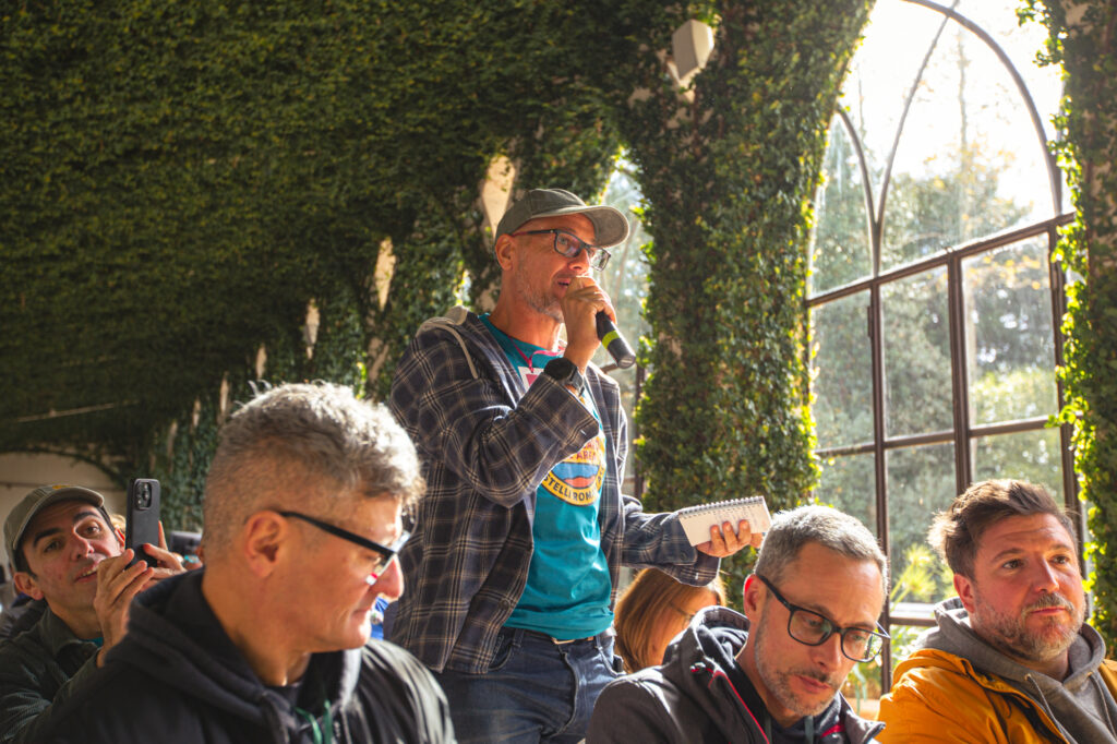 Appassionati di mountain bike ascoltano una presentazione in un ambiente luminoso e verdeggiante.