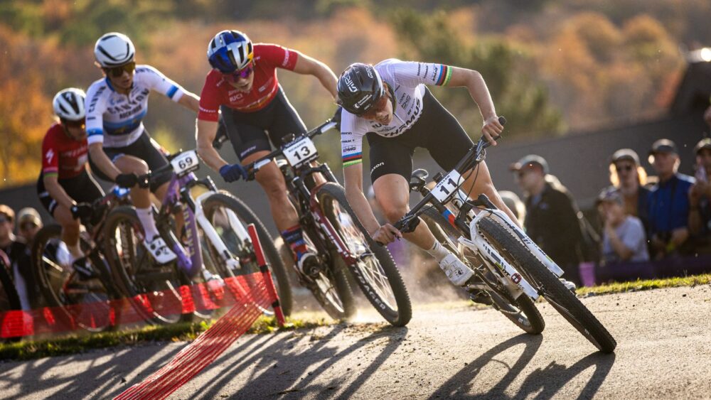 Ciclisti in gara durante una competizione di mountain bike, curve e velocità in un contesto naturale.