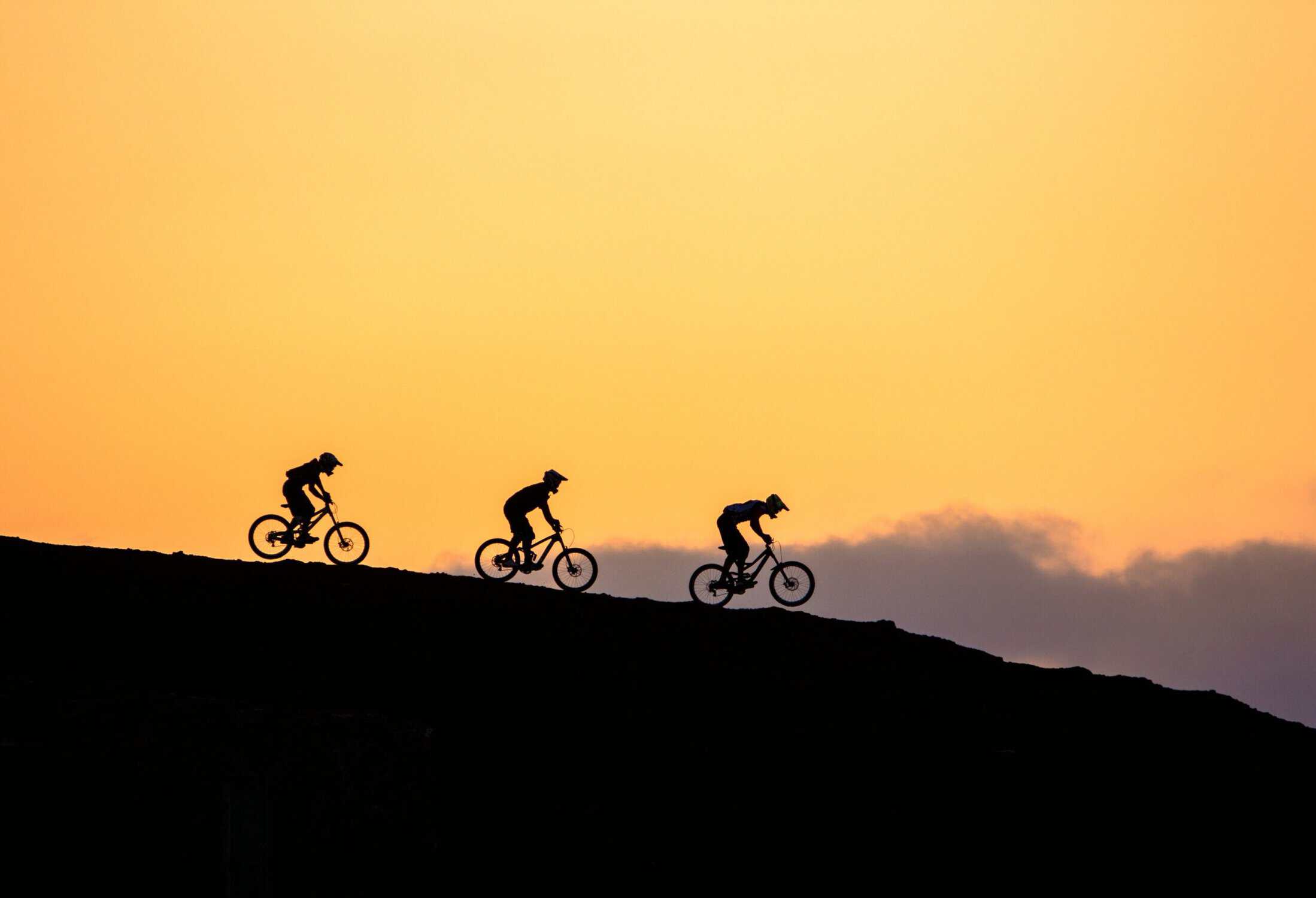 Silhouette di ciclisti in mountain bike al tramonto su una collina.