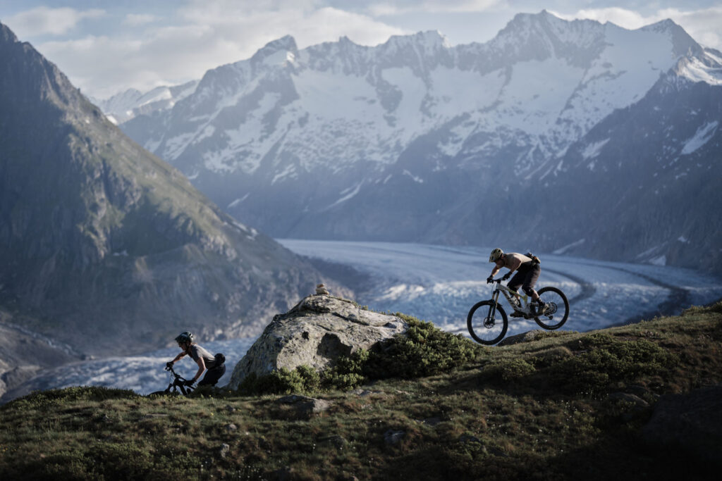 Vignetta di due mountain bikers su un sentiero tra montagne e ghiacciai.