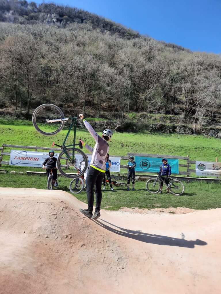 Ragazzo fa acrobazia in mountain bike su un pump track all'aperto in montagna.