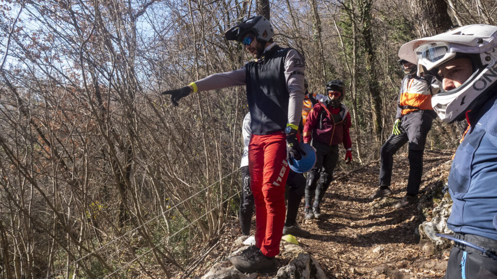 Guida in mountain bike in un sentiero boschivo con bikers equipaggiati di caschi e protezioni.