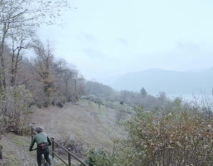 Ciclista su sentiero montano tra gli alberi autunnali con vista sulle colline lontane.
