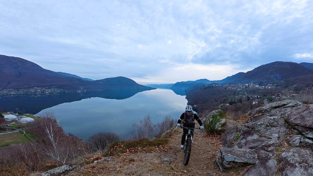 VTT su sentiero panoramico con vista lago e montagne in autunno, avventura e sport all'aperto.