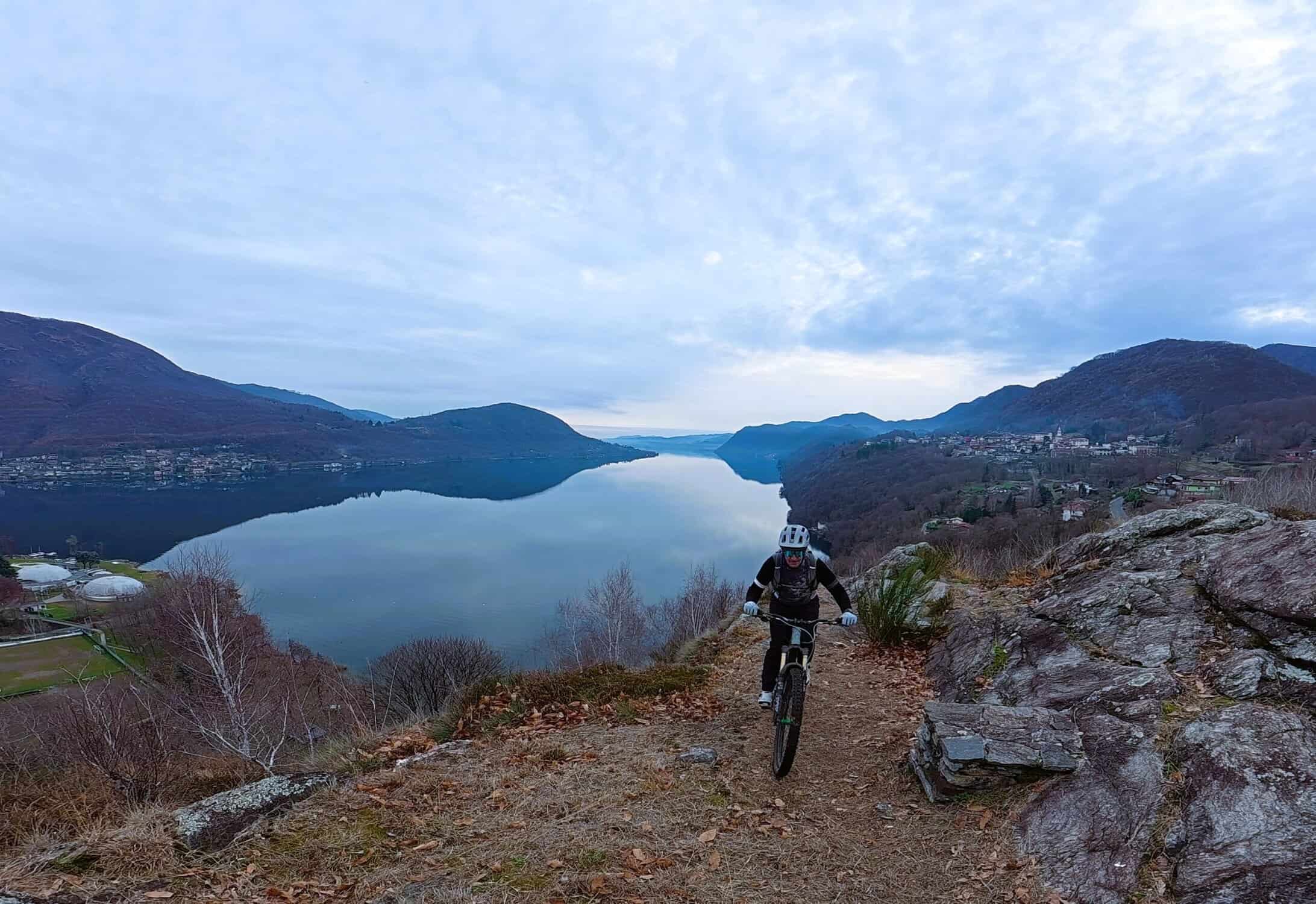 VTT su sentiero panoramico con vista lago e montagne in autunno, avventura e sport all'aperto.