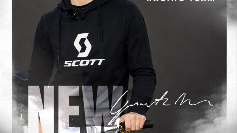 Scott Racing Team rider promoter a mountain bike con logo e firma sullo sfondo nuvoloso.