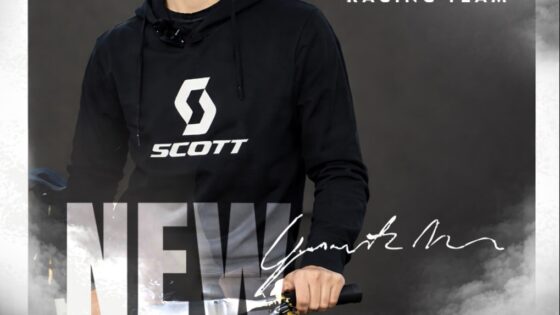 Scott Racing Team rider promoter a mountain bike con logo e firma sullo sfondo nuvoloso.