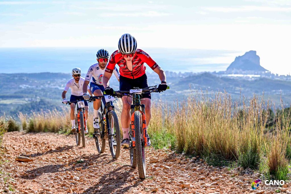 Montagna, ciclisti su sentiero in natura con vista mare e rocca di sfondo.