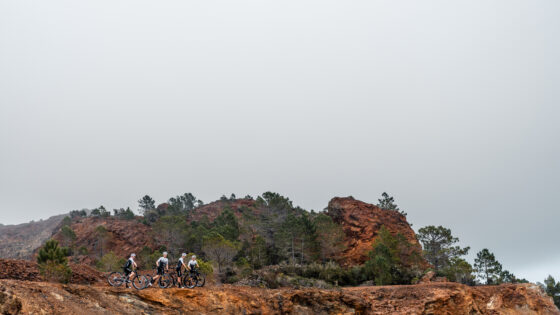 Escursionisti in mountain bike su un sentiero roccioso in un paesaggio arido e pieno di rocce rosse con pini sparsi.